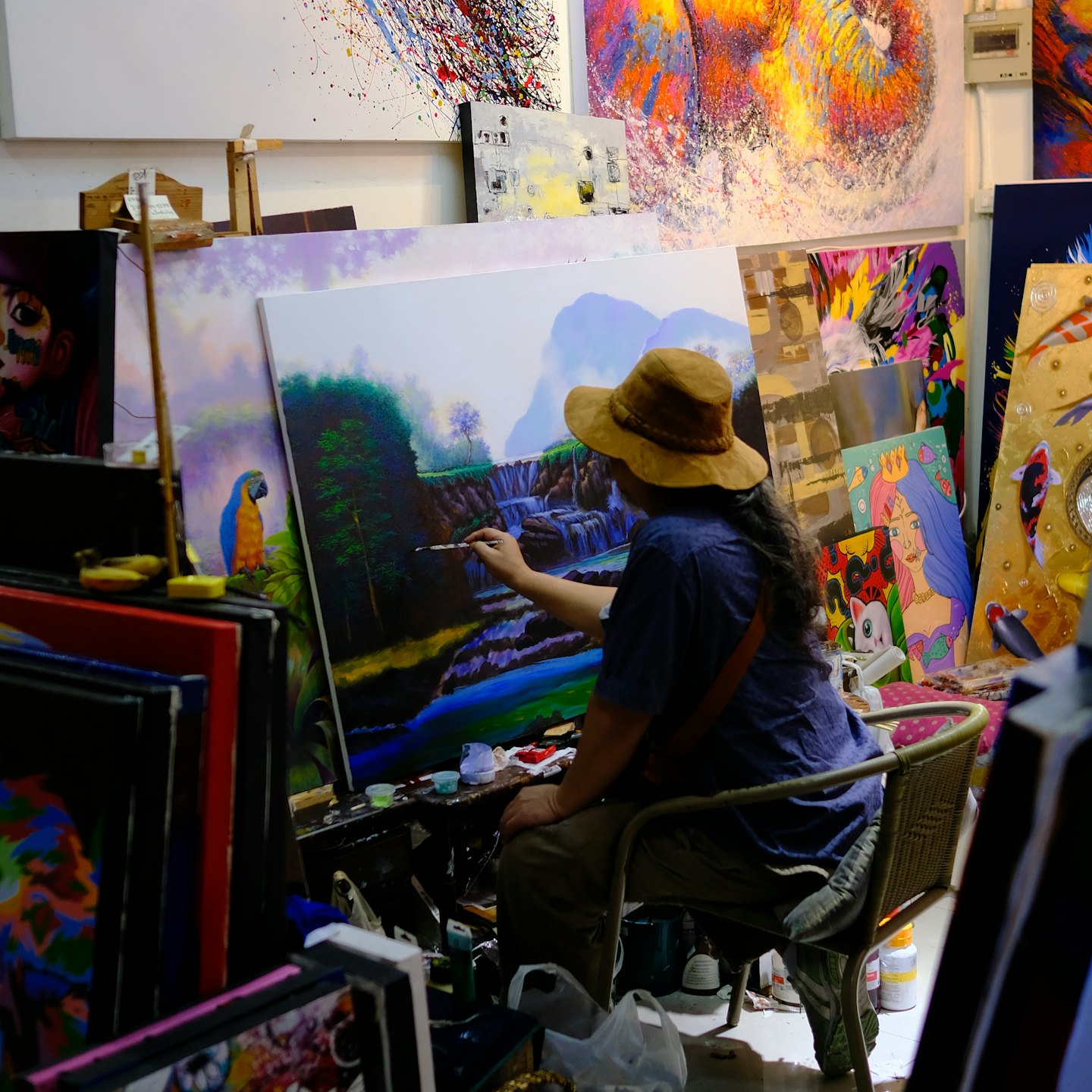 An artist paints a landscape of a waterfall on an easel.