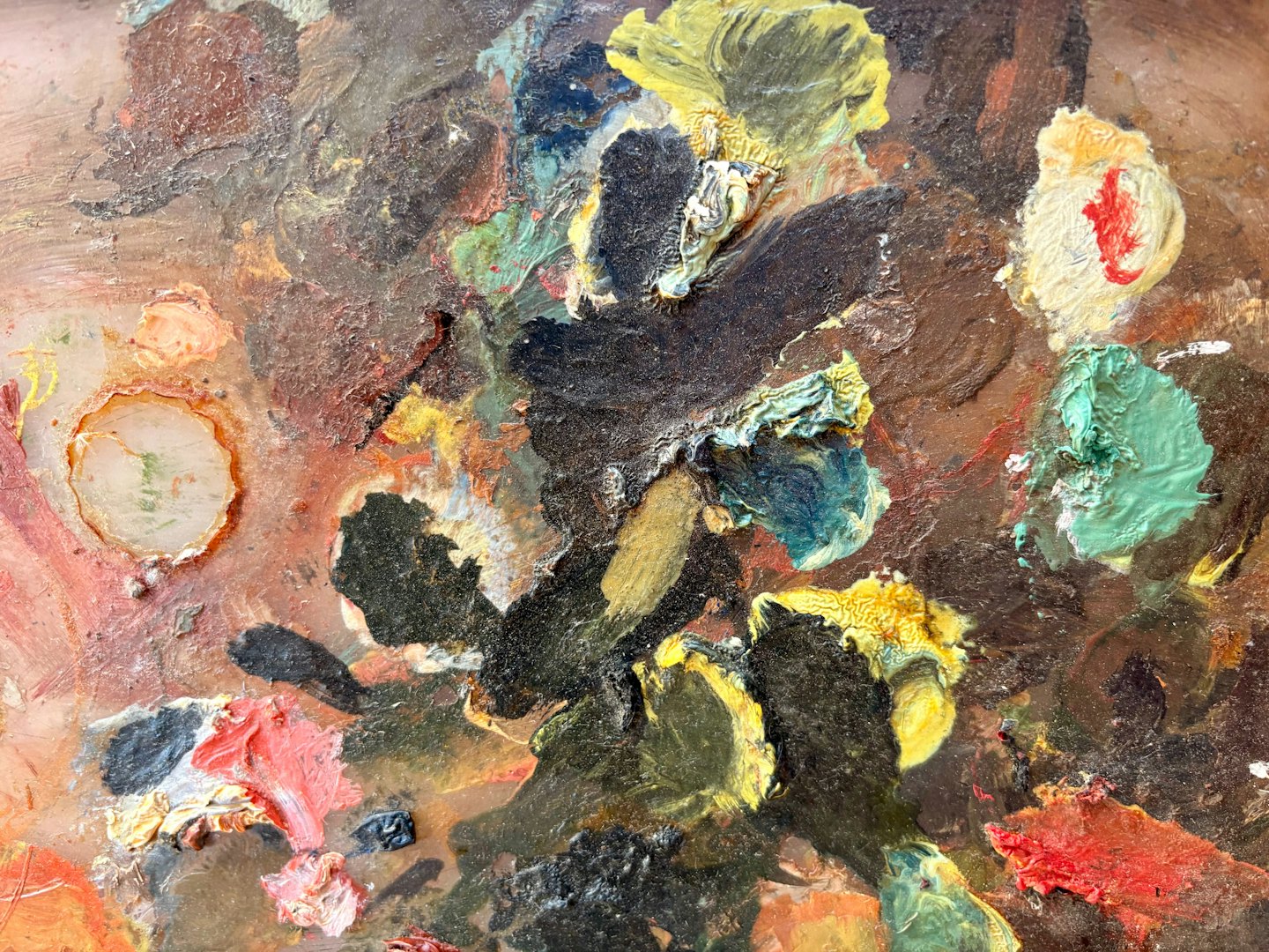 Wooden artist palette covered in layers of colorful oil paint.
